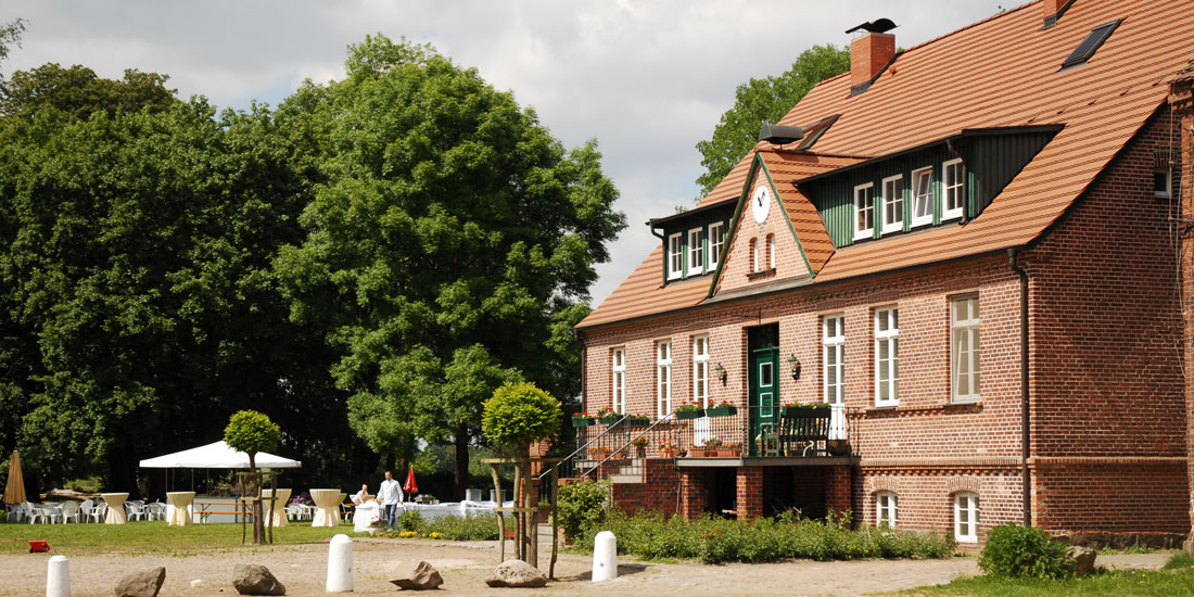 Gutshaus mit Backsteinfassade, alter Baum und Hof